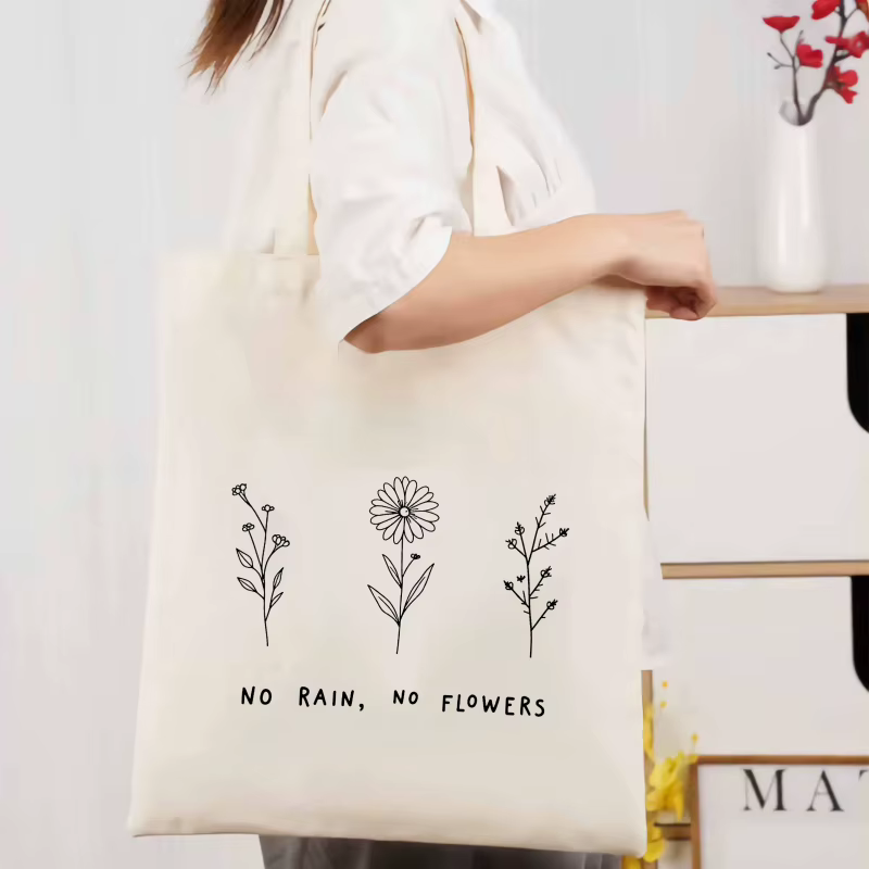 Sac fourre-tout en coton à motif floral crème et texte "No Rain No Flower", adapté à un usage quotid